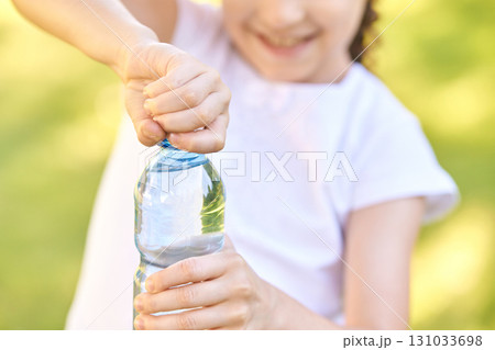 Young caucasian girl opening water bottle in park on sunny day, focused Young caucasian girl opening water bottle in park on sunny day, focused 131033698