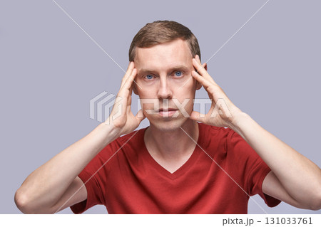 Caucasian male adult holding head in red shirt on gray background Caucasian male adult holding head in red shirt on gray background 131033761