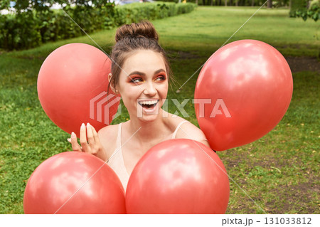 Young caucasian adult female smiling surrounded by red balloons in green Young caucasian adult female smiling surrounded by red balloons in green 131033812