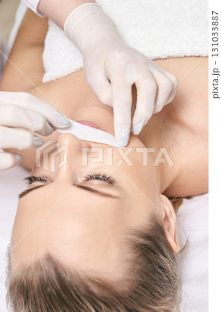 Caucasian female adult undergoing lip hair removal with wax strip by beautician 131033887