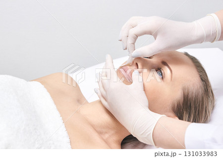 Caucasian female adult receiving cosmetic facial treatment by gloved hands 131033983