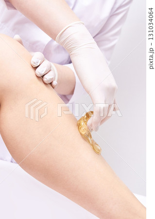 Female leg sugaring hair removal technique with gloved hands in beauty salon 131034064