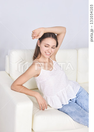 Smiling young caucasian female relaxing on white sofa in casual outfit Smiling young caucasian female relaxing on white sofa in casual outfit 131034103
