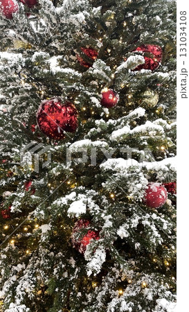 Snowy Christmas tree with red ball and lights garland. Urban city decoration at street. Xmas holiday pattern. Cold winter weather. Outdoors. Snowy Christmas tree with red ball and lights garland. Urban city decoration at street. Xmas holiday pattern. Cold winter weather. Outdoors. 131034108