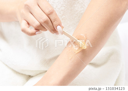 Female caucasian adult applying wax on arm for hair removal using wooden 131034123