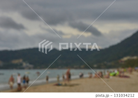 Blurry beach scene with cloudy sky and people enjoying the shoreline 131034212