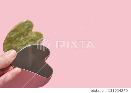 Gua sha tools: green jade and stainless steel massage stone set on soft pink Gua sha tools: green jade and stainless steel massage stone set on soft pink 131034279