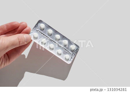 Hand holding blister pack with white tablets against light gray background Hand holding blister pack with white tablets against light gray background 131034281
