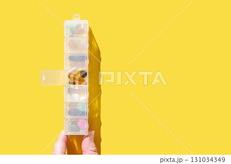 Hand holding transparent pill organizer with various supplements on bright Hand holding transparent pill organizer with various supplements on bright 131034349