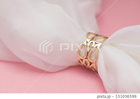 A gold ring with a flower design sits on a white cloth A gold ring with a flower design sits on a white cloth 131036599