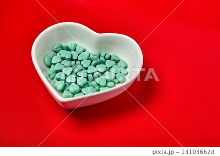 turquoise colored cardiology pills in white ceramic heart shaped bowl on red background 131036628