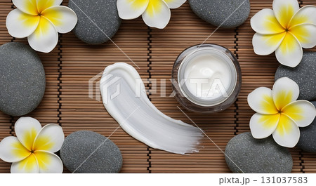 Luxurious skincare cream swirl with spa stones and plumeria flowers on bamboo mat 131037583