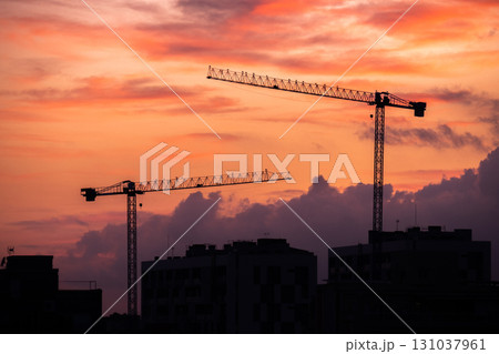 Silhouettes of construction cranes against a vibrant sunset sky. The scene captures the essence of urban development and industrial growth. Silhouettes of construction cranes against a vibrant sunset sky. The scene captures the essence of urban development and industrial growth. 131037961