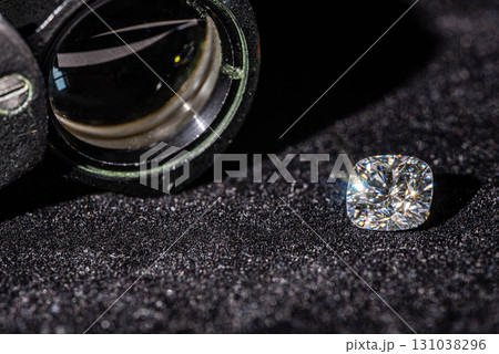 A diamond is on a black surface next to a magnifying glass A diamond is on a black surface next to a magnifying glass 131038296