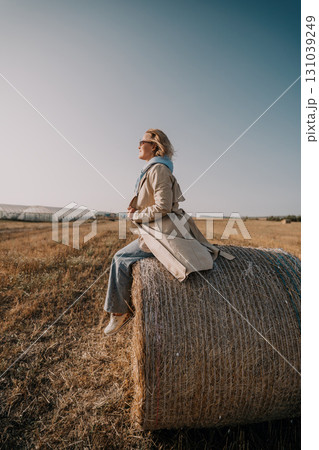 Woman Sitting on Hay Bale in Field 131039249