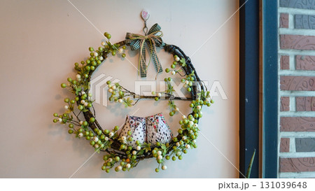 Charming rustic wreath with cute fabric owls and green berries on a light wall, cozy home decor Charming rustic wreath with cute fabric owls and green berries on a light wall, cozy home decor 131039648