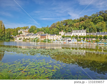 Picturesque Pierrefonds village in Oise, France, lines a tranquil lake with reflections of its charming buildings. Lily pads dot the water, and small boats are moored near a lively lakeside restaurant Picturesque Pierrefonds village in Oise, France, lines a tranquil lake with reflections of its charming buildings. Lily pads dot the water, and small boats are moored near a lively lakeside restaurant 131039857