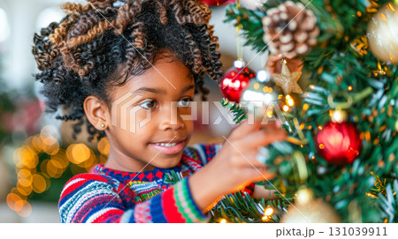 Young girl with curly hair decorating Christmas tree with colorful ornaments and festive lights 131039911