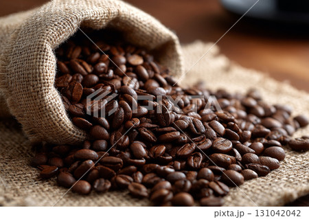 Roasted coffee bean spilling from burlap sack onto coarse sackcloth, rich aroma and warm brown tones evoke cozy morning energy 131042042