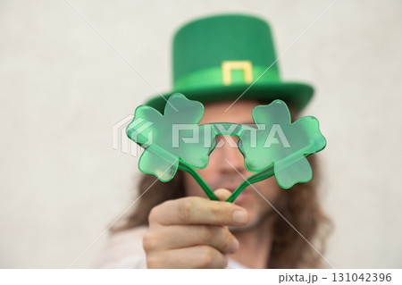 Happy Man with funny Shamrock clover glasses and Green St. Patrick's Hat against beige wall. Close up. Happy Man with funny Shamrock clover glasses and Green St. Patrick's Hat against beige wall. Close up. 131042396