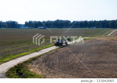 A large tractor is driving steadily down a dirt road in an open field 131042665