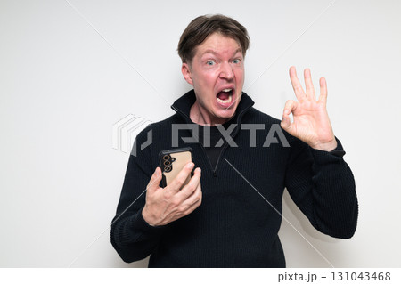 Scandinavian mid adult man using phone against white background making OK sign gesture 131043468