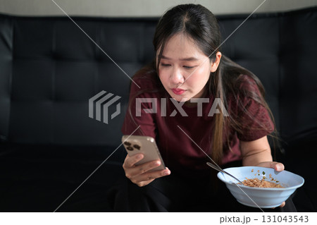 Asian woman sitting at home in sofa eating instant noodles from bowl Asian woman sitting at home in sofa eating instant noodles from bowl 131043543