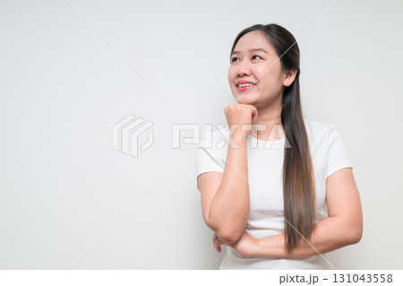 Portrait of young Asian woman with hand on chin planning and looking up against white background 131043558