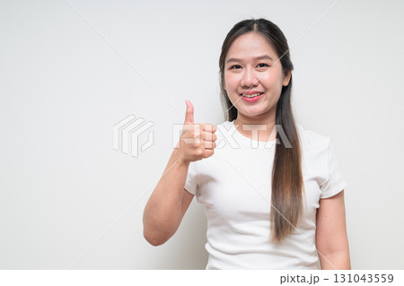 Portrait of young Asian woman smiling and giving thumbs up against white background 131043559