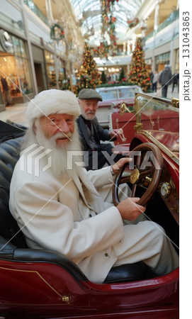 An Elderly Man in a White Suit and Santa Hat Sits Behind the Wheel of a Vintage Car With a Friend Beside Him 131043863