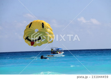 yellow parachute with a smiley face design floats above the turquoise sea 131044459