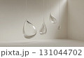Translucent teardrop glass sculptures suspended from white ceiling, creating ethereal light play within minimalist interior space with pristine walls and flooring 131044702