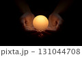 Luminous glowing sphere nestled in cupped hands, radiating warmth and potential against shadowy background, representing innovative thinking and human connection 131044708