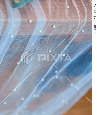 Close-up of a sheer fabric panel adorned with elegant pearl embellishments. The soft texture and intricate detailing create a delicate, captivating visual element, perfect for design inspiration 131045073