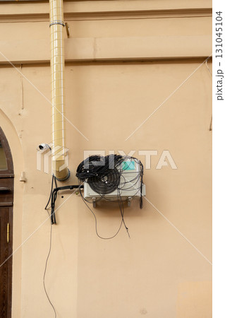 An air conditioner with large coil of wires for connection is installed on facade of the house.  131045104