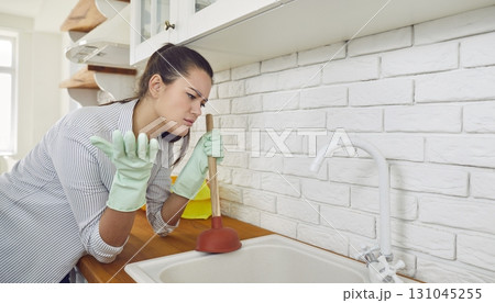 Woman doing work about the house and trying to unclog the blockage in the kitchen sink Woman doing work about the house and trying to unclog the blockage in the kitchen sink 131045255