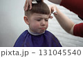 child squinting during haircut at barber 131045540