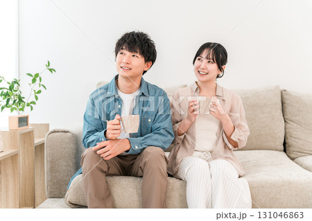 ソファでホットドリンクを飲みながらくつろぐ若いカップル,夫婦 131046863