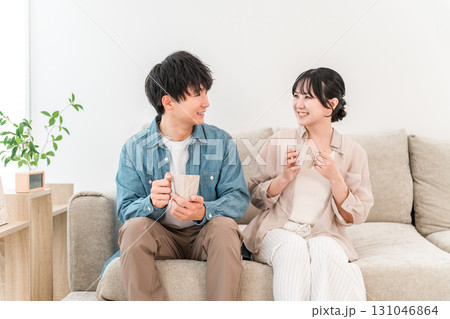 ソファでホットドリンクを飲みながらくつろぐ若いカップル,夫婦 131046864