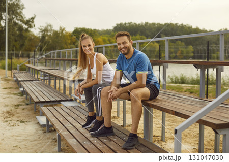 Sporty couple in sportswear sitting in city park and looking at camera after sport exercises. 131047030