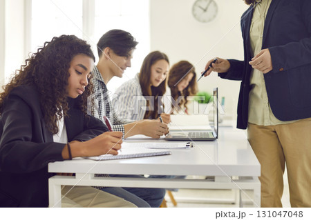 Group of young students writing test with teacher during a lesson in the classroom. 131047048