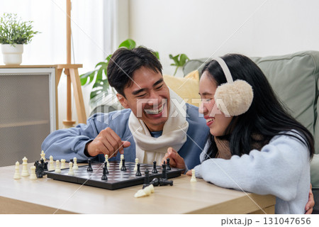 Winter couple, happy people, enjoy indoor day at home, playing lively game of chess, sharing laughter and warmth, cozy winter atmosphere fills living space, creating joyous memories. Winter couple, happy people, enjoy indoor day at home, playing lively game of chess, sharing laughter and warmth, cozy winter atmosphere fills living space, creating joyous memories. 131047656