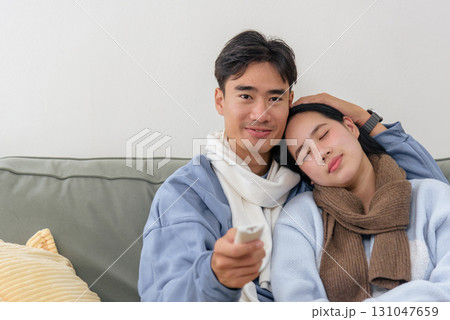 Winter finds happy couple relaxing comfortably at home, enjoying quiet day together. Man holds television remote control, woman rests head peacefully on his shoulder, embracing warmth winter cold. Winter finds happy couple relaxing comfortably at home, enjoying quiet day together. Man holds television remote control, woman rests head peacefully on his shoulder, embracing warmth winter cold. 131047659