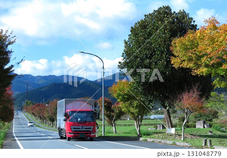秋晴れの山間地、真っ直ぐな道路と、走行してくる赤いトラック 131048779