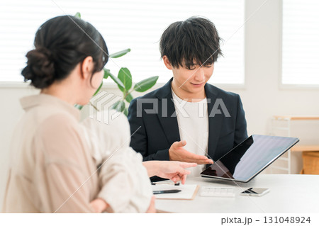 タブレットを使い赤ちゃんを抱く女性客に説明をする営業マンの男性 131048924