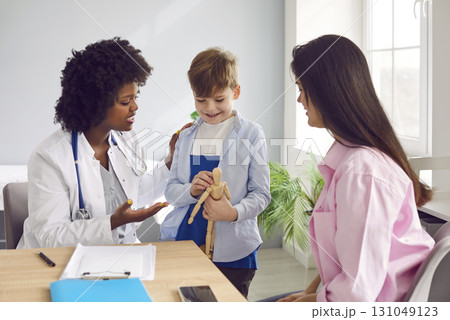 Caring female pediatrician talking to small boy patient and his mother in hospital 131049123