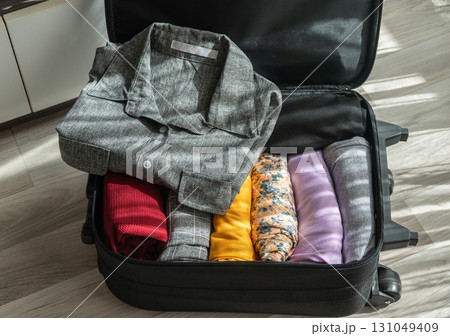 An opened suitcase with colorful clothings pack and arrange inside. An opened suitcase with colorful clothings pack and arrange inside. 131049409