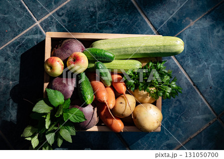 Freshly collected vegetables and fruits in a wooden basket arranged on a tiled floor in natural light Freshly collected vegetables and fruits in a wooden basket arranged on a tiled floor in natural light 131050700