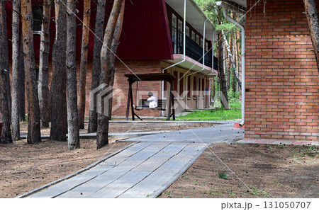 Individual sitting on a bench in a quiet wooded area near a brick building during daylight hours Individual sitting on a bench in a quiet wooded area near a brick building during daylight hours 131050707