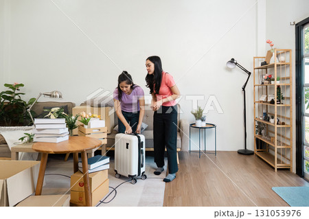 Two women unpacking boxes and organizing luggage in their living room, working together to create a cozy and welcoming home. 131053976